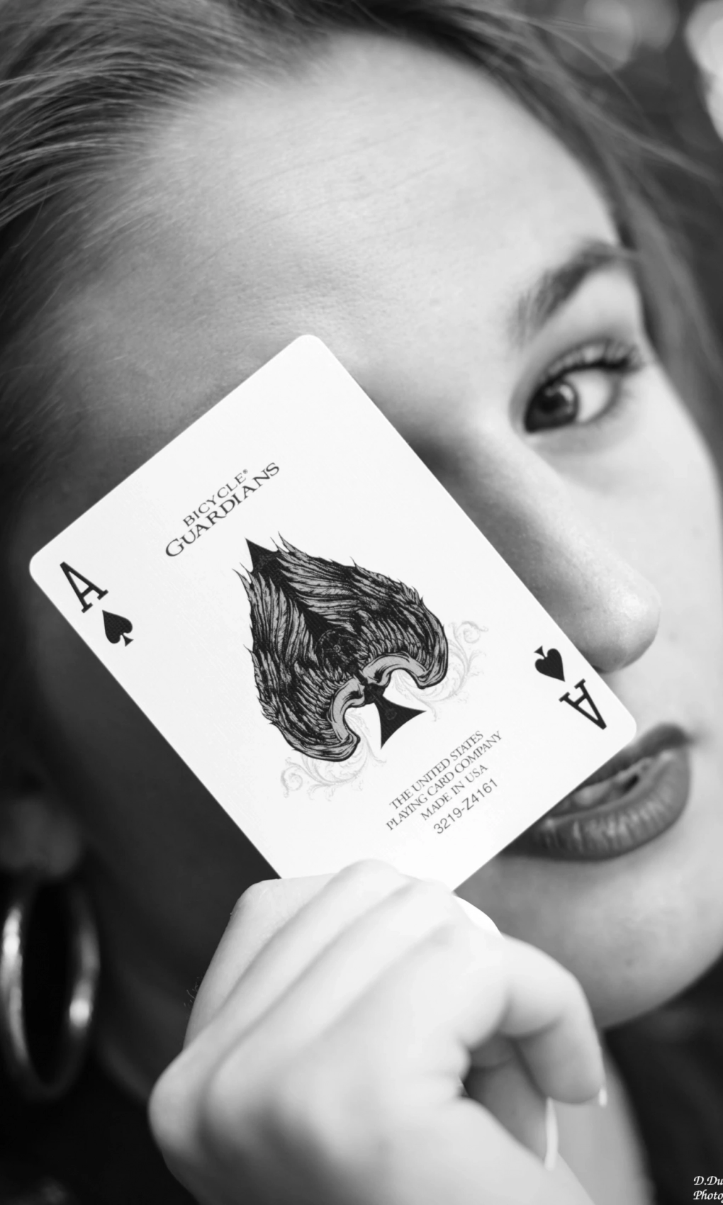 Photo en noir et blanc prise durant une séance photo. La modèle tient une carte (un as de pique) devant son oeil. Une photo original, pour un shooting original, et un moment original.