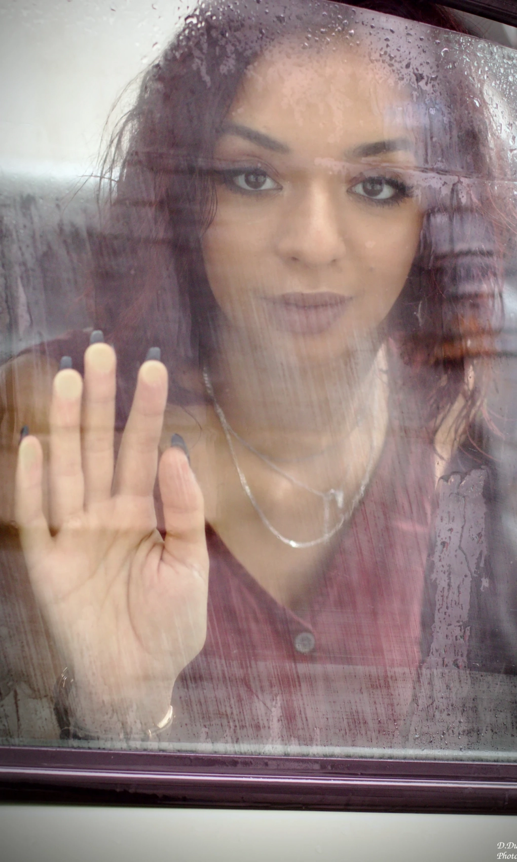 Photo prise à travers une vitre de voiture durant la pluie lors d'une séance photo. On voit la modèle de l'autre côté avec sa main contre la vitre.